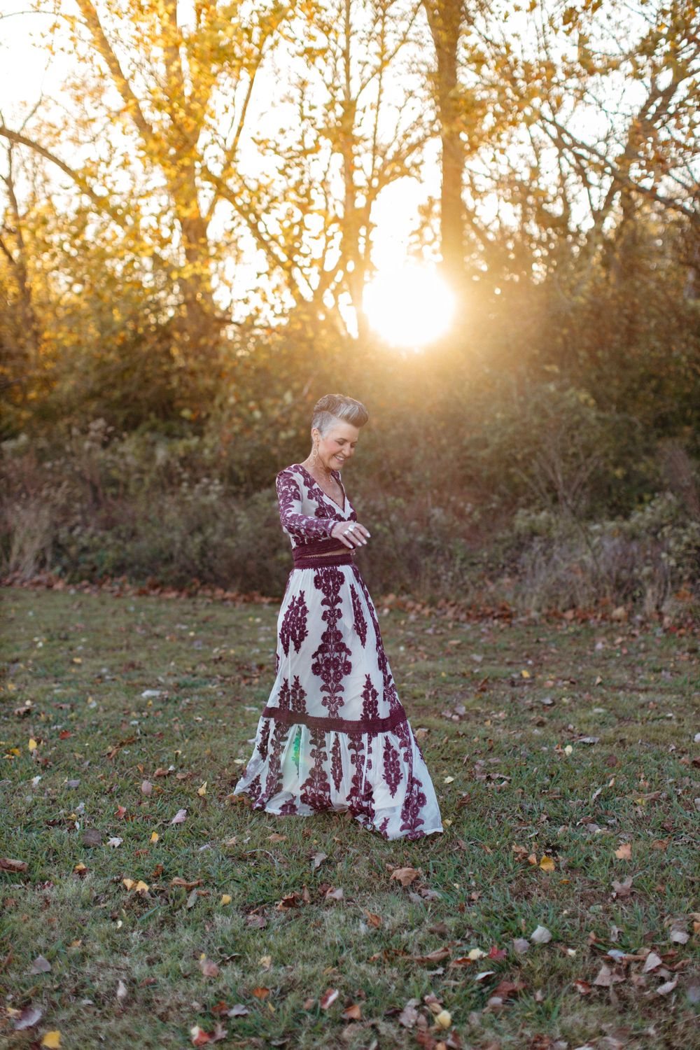 Elegant burgundy dress silhouetted against golden sunset in autumn landscape.