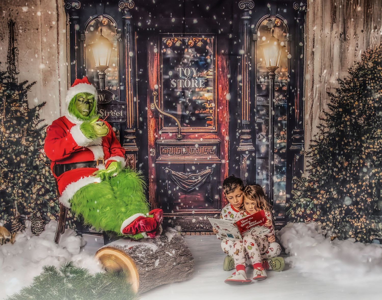 The Green guy in Santa costume sitting by a snowy storefront with Christmas decorations and lights.