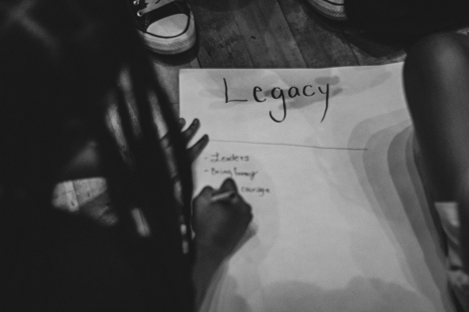 Black and white image of hands writing the word Legacy on paper.