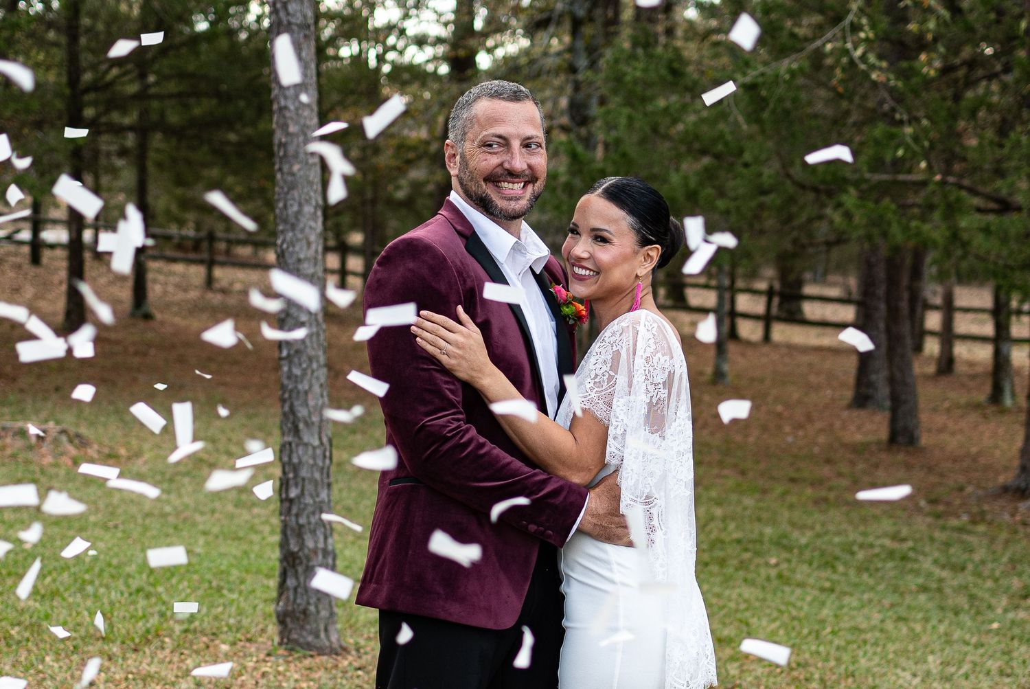 Newlyweds celebrating with confetti shower in burgundy suit and white wedding dress.