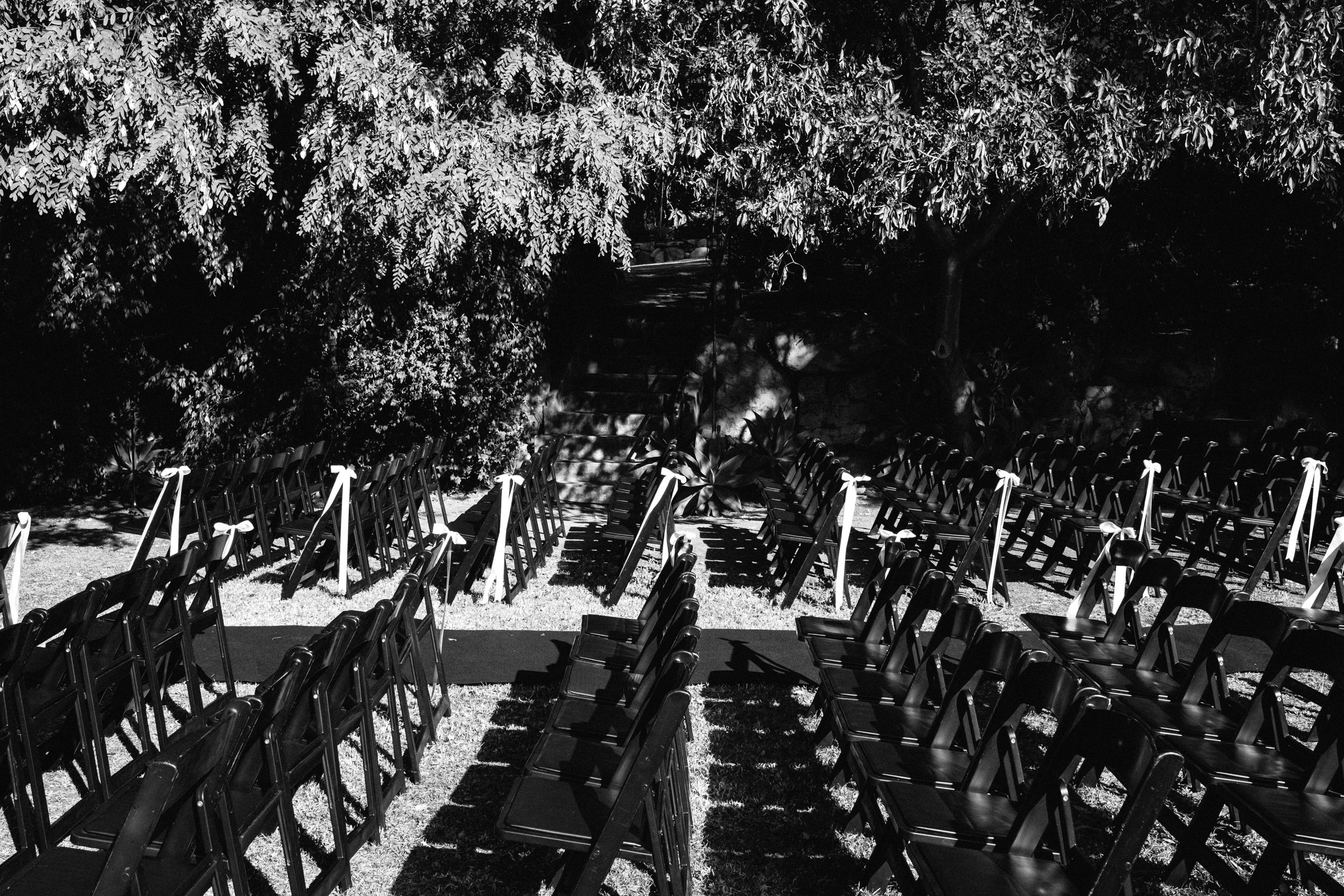 Black and white aerial view of empty wedding ceremony chairs arranged in rows outdoors.
