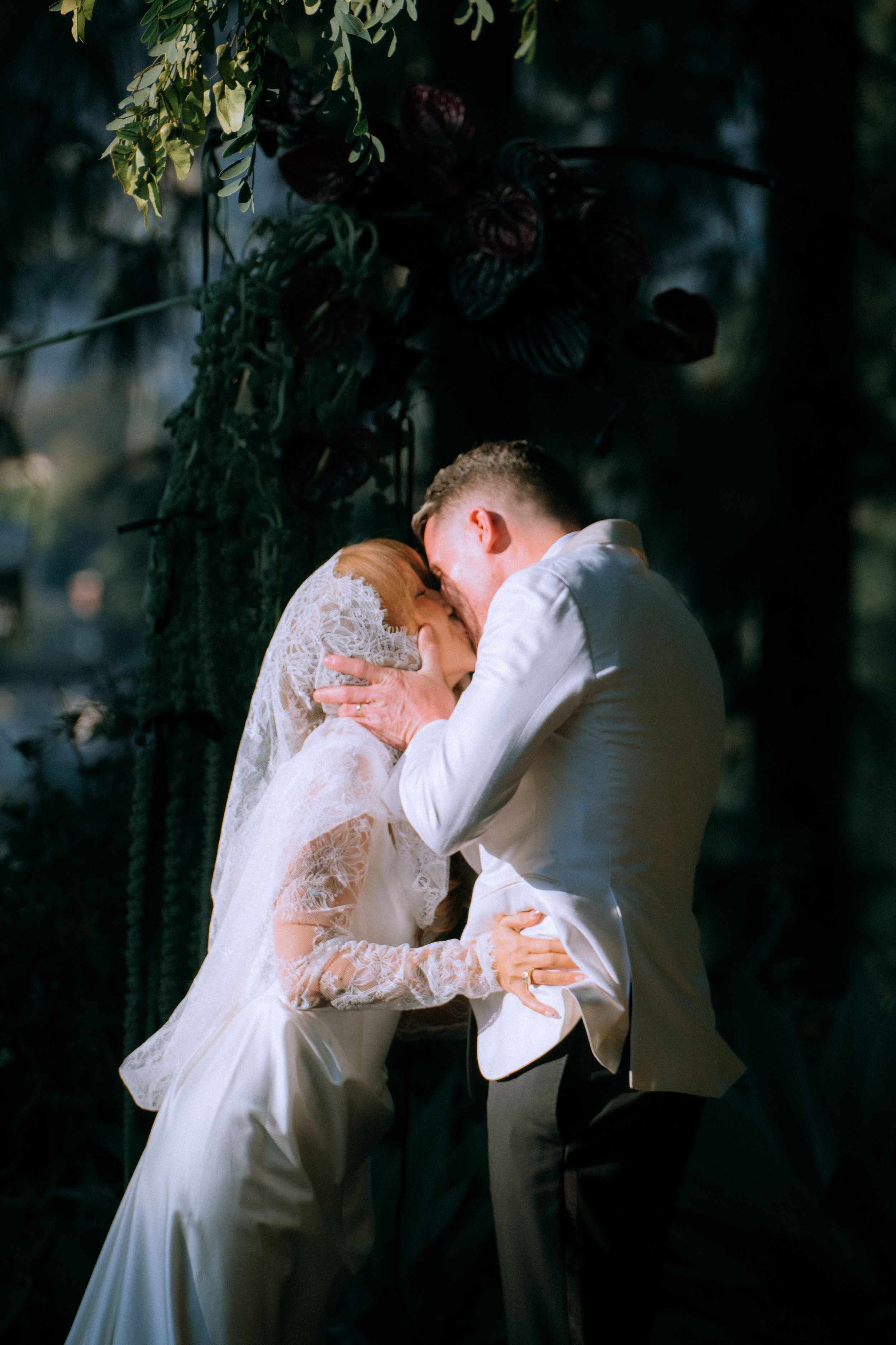 Intimate wedding portrait of a couple embracing under garden foliage at dusk.