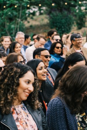 Wedding guests smile and laugh during outdoor reception celebration.