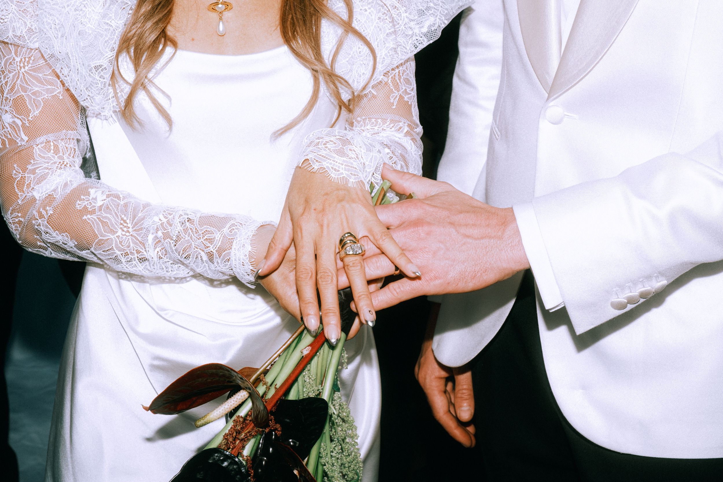 Close-up shot of newlyweds' hands with wedding rings and bridal bouquet.