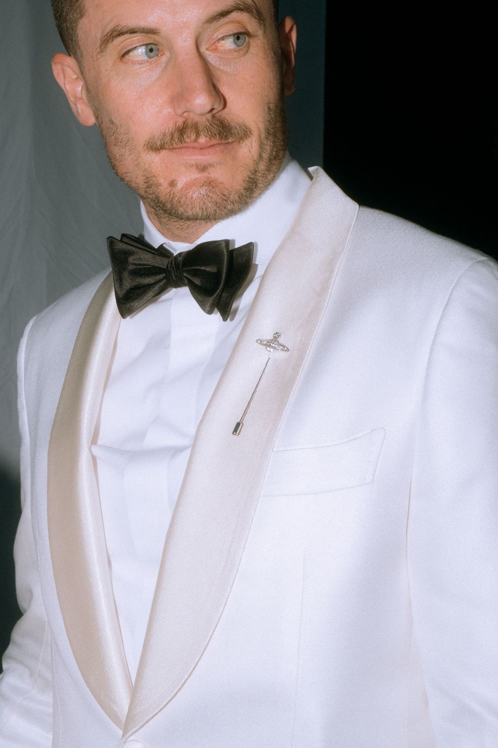 Close-up of formal white tuxedo jacket with black bow tie and lapel pin.