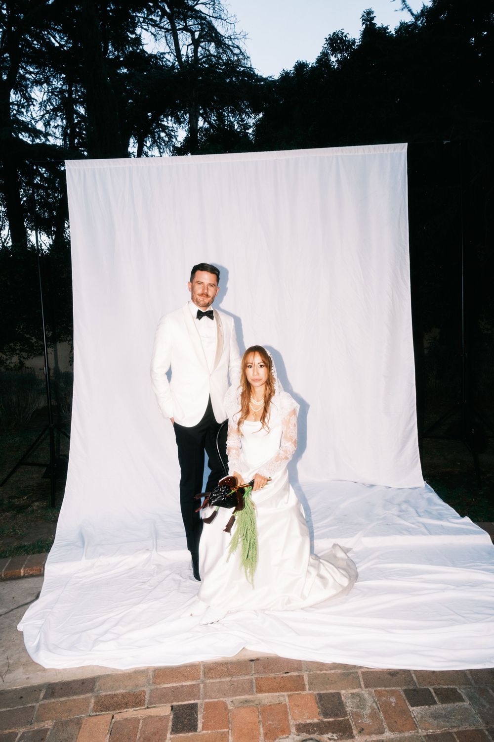 Couple poses against white backdrop in formal wedding attire.