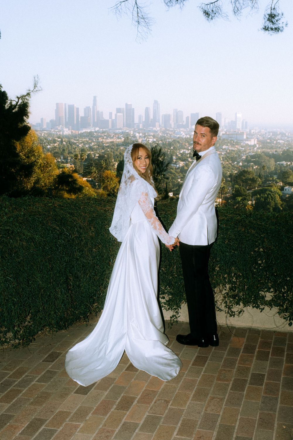 Couple in wedding attire poses with downtown skyline view.