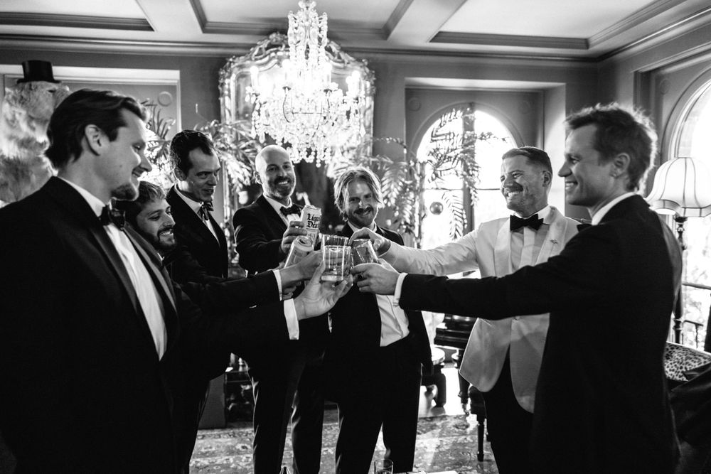 Groomsmen toast with drinks under crystal chandelier at formal wedding reception.