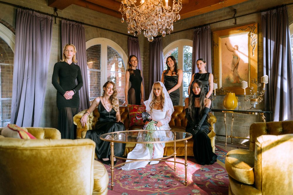 Wedding party poses elegantly in luxurious room with chandelier and gold decor.