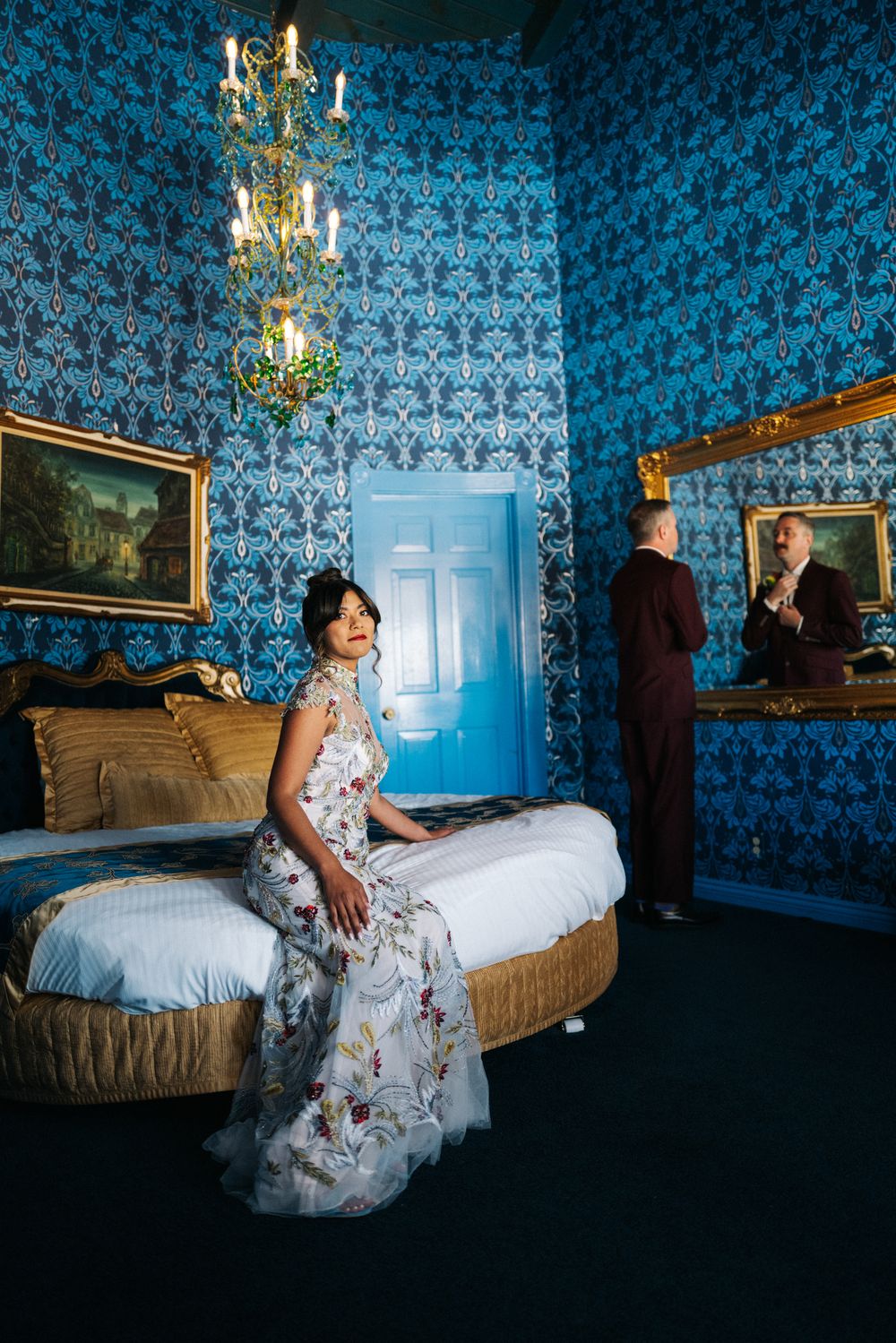 Elegant wedding scene in blue baroque room with ornate wallpaper, chandelier, and vintage decor.