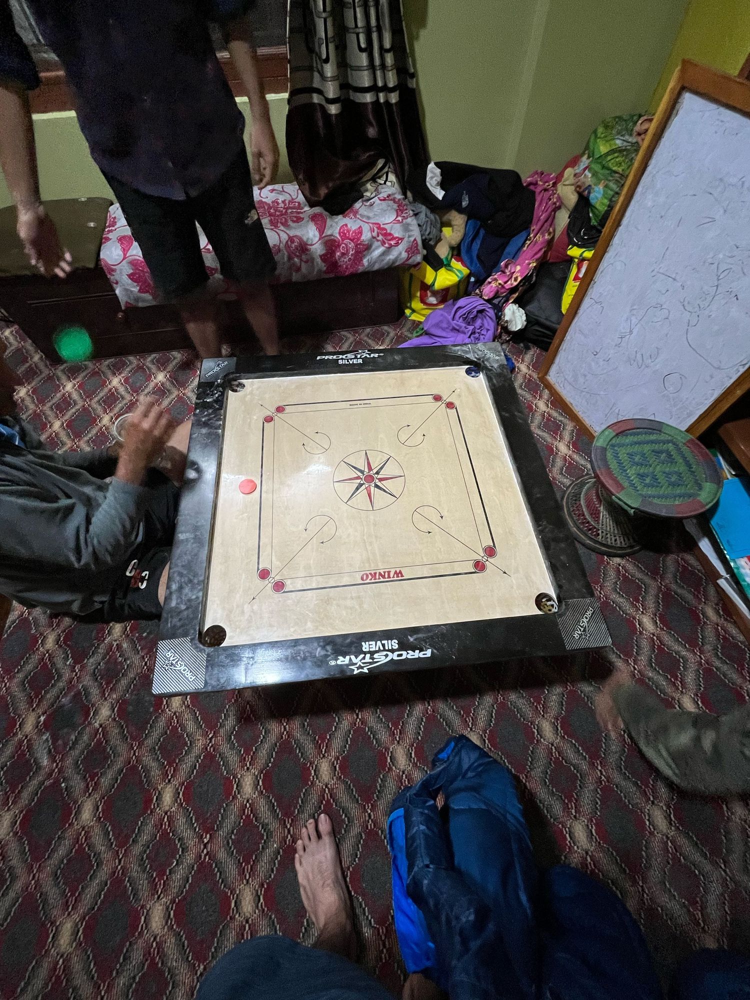 Carrom board game setup on a patterned surface with scattered game pieces.