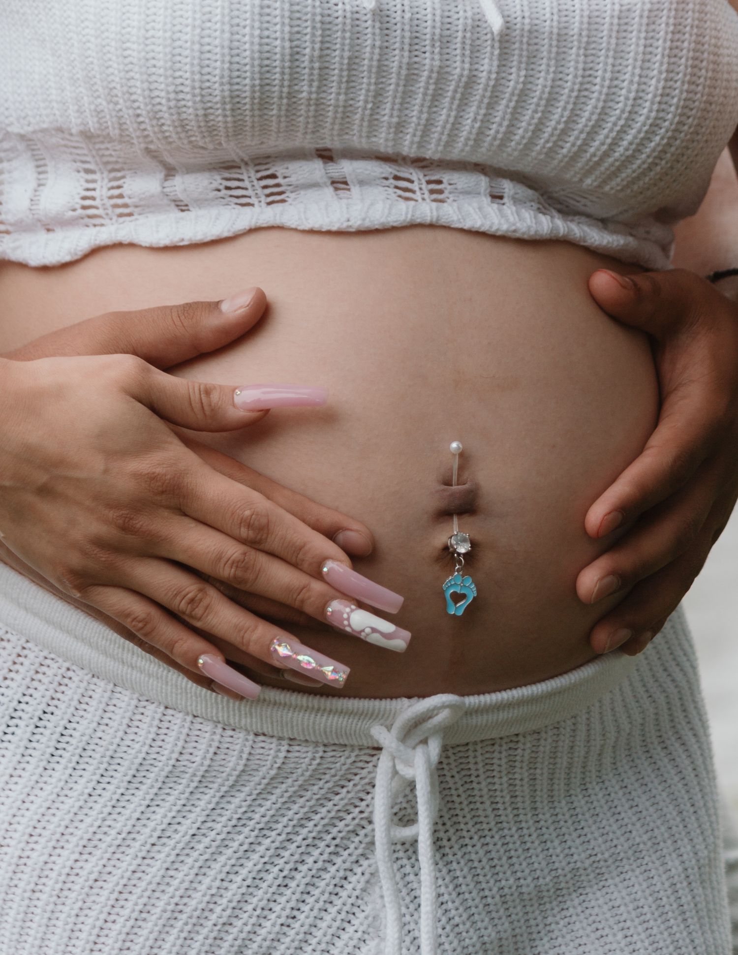 Close-up of exposed midriff wearing white knit clothing showing decorative belly button piercing with blue charm.