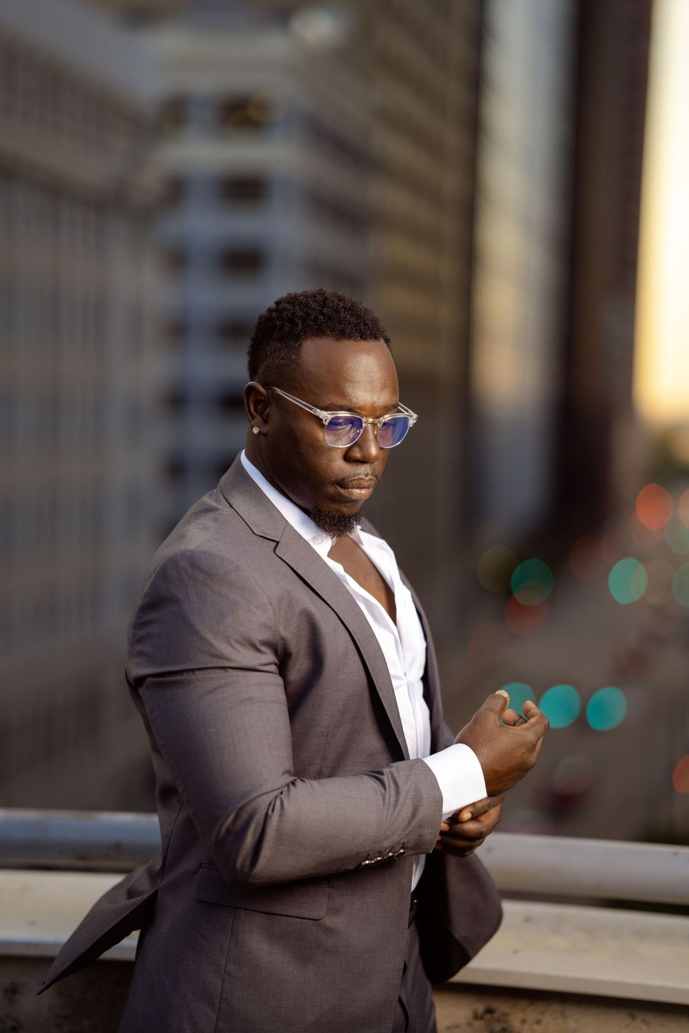 Professional wearing a gray suit and glasses checks their phone in an urban setting during golden hour.
