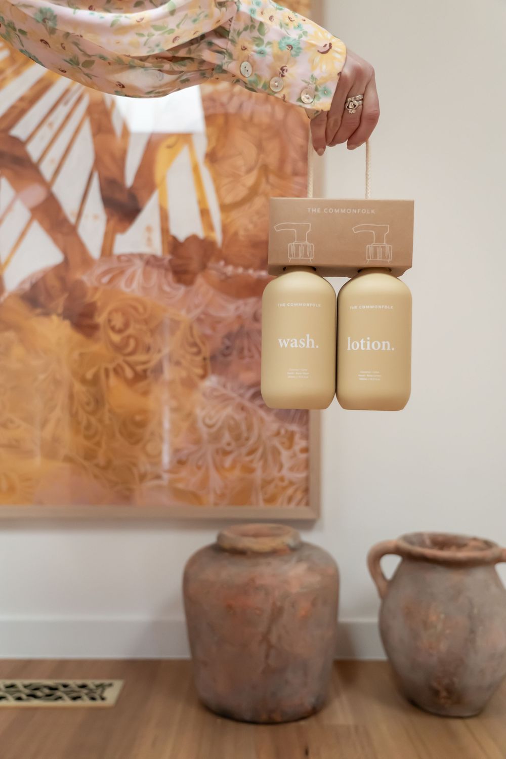 Beige pump bottles displayed against a warm-toned wall with vintage ceramic vessels below.