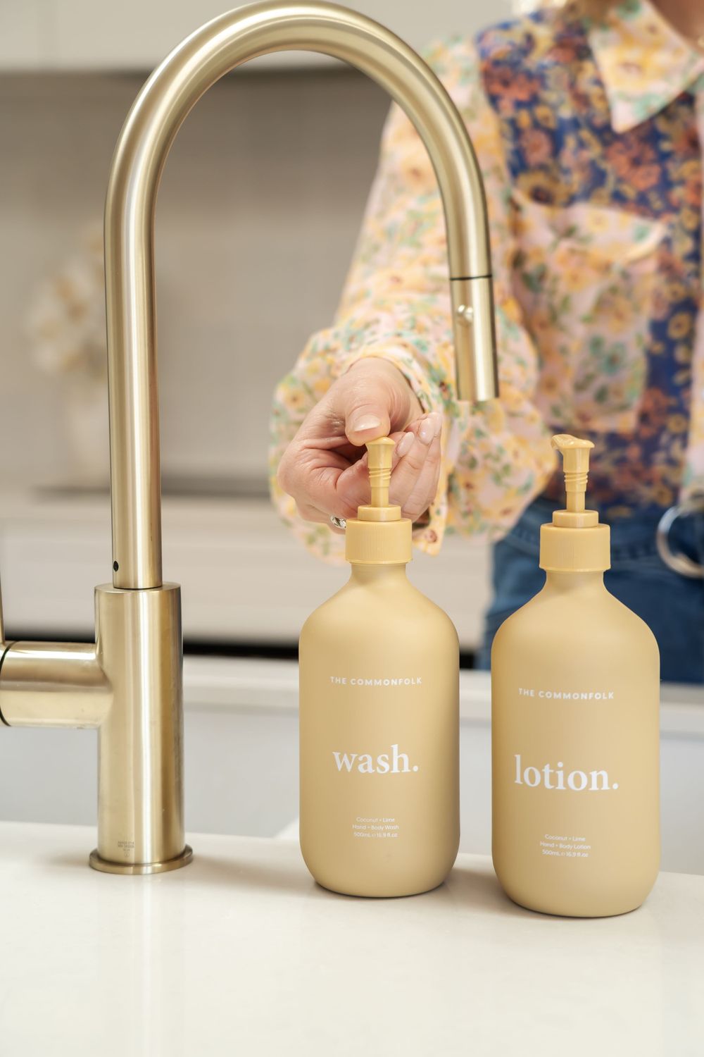 Gold faucet and beige pump dispensers labeled wash and lotion on white countertop.