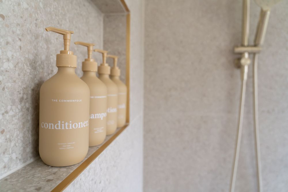 Row of neutral beige refillable soap dispensers on a bathroom shelf against a textured wall.