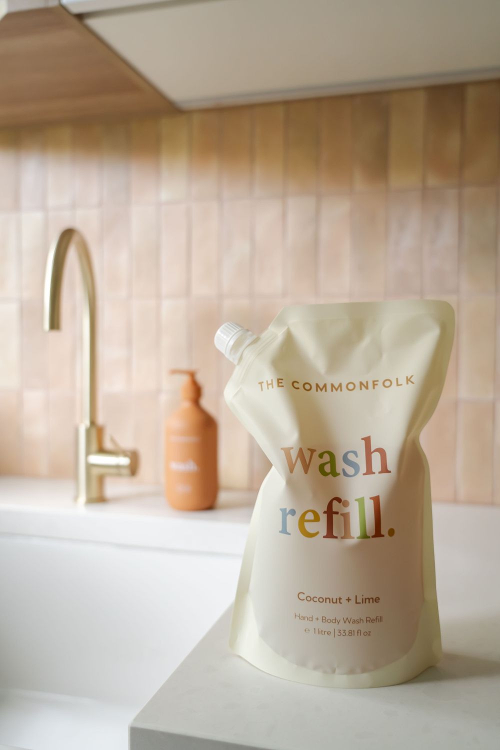 Refillable wash pouch from The Commonfolk brand displayed near brass faucet in modern bathroom.