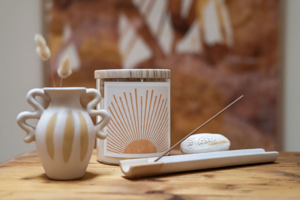 White ceramic vase and sunburst patterned candle arranged on wooden surface with incense holder.