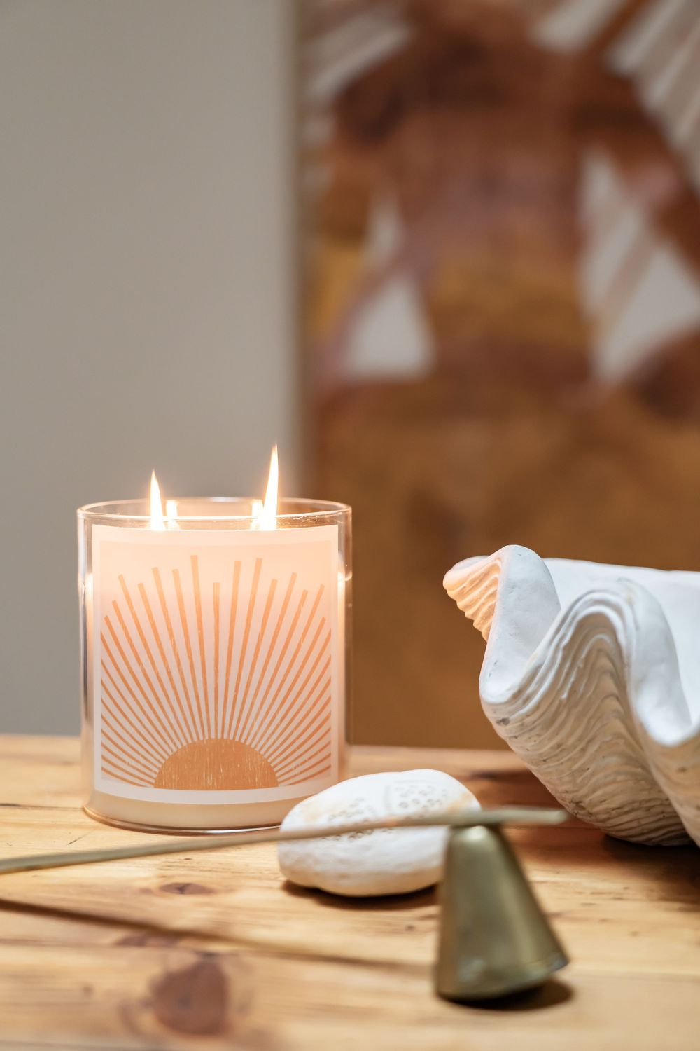 Lit candle with sunburst design next to white ceramic shells on wooden surface.