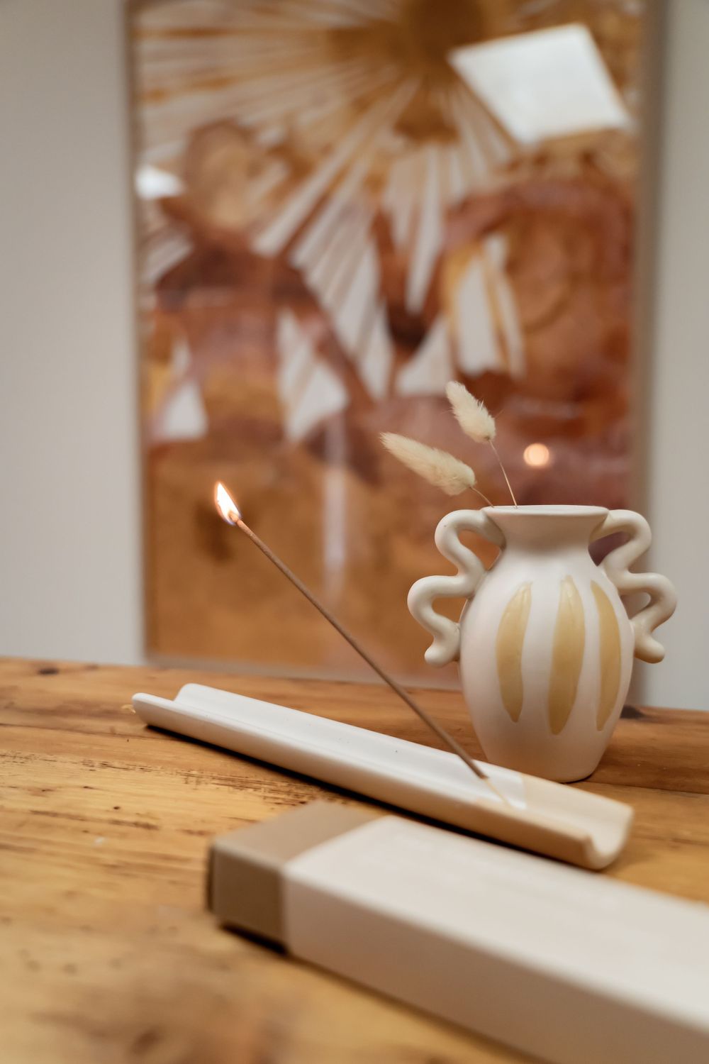 An incense holder with burning incense stick next to a decorative striped vase on a wooden surface.