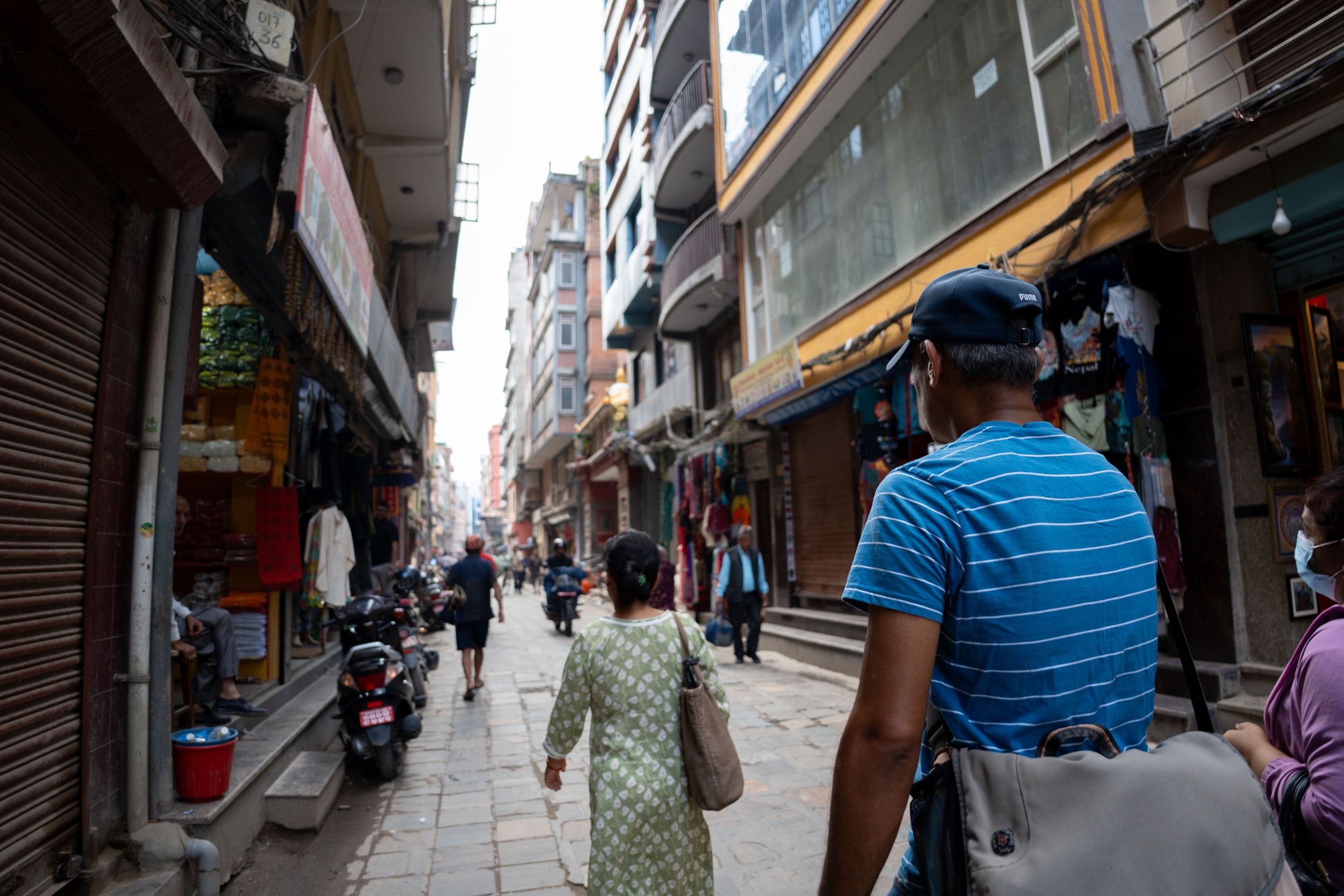 Narrow urban street lined with tall buildings and scattered pedestrians.