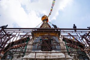 Ancient stupa undergoing restoration with scaffolding and prayer flags in Kathmandu.