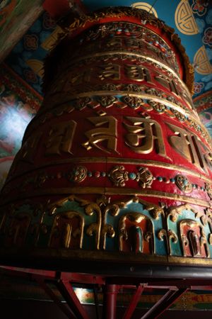 Large cylindrical prayer wheel with intricate gold Tibetan script on red background.