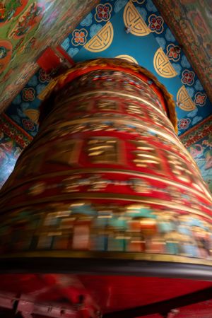 Spinning prayer wheel creating motion blur against blue and red decorated ceiling.