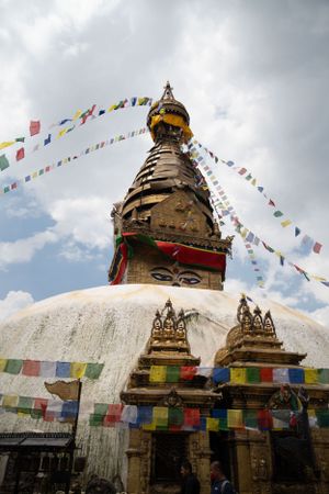 White Buddhist stupa with colorful prayer flags under cloudy sky at Swayambhunath.