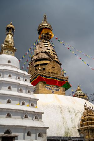 Historic Buddhist temple complex with white stupas and prayer flags against stormy sky.