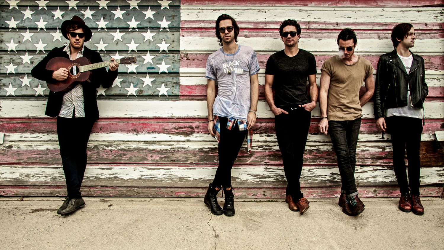 country music band portrait Terraplane Sun members standing against weathered American Flag painted on garage door lead singer with guitar