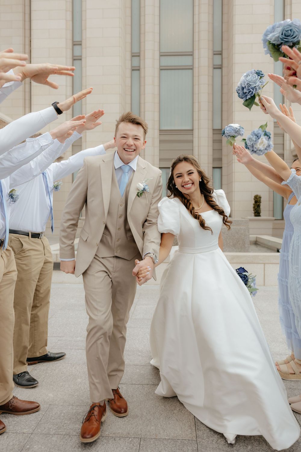 Smiling bride and groom walk through arch of raised hands formed by their wedding party.