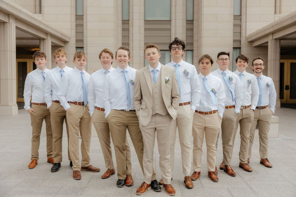 Groom in tan suit standing with groomsmen in khaki pants and light blue ties outside a temple.