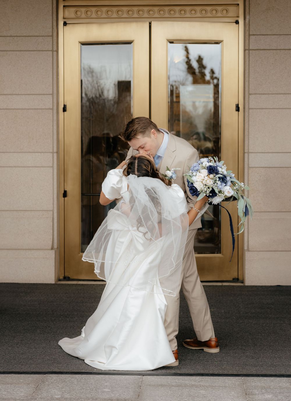Groom dips bride in a romantic kiss in front of golden temple doors on wedding day.