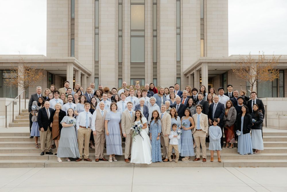 Large wedding party group photo on steps of a grand building with family and guests celebrating.
