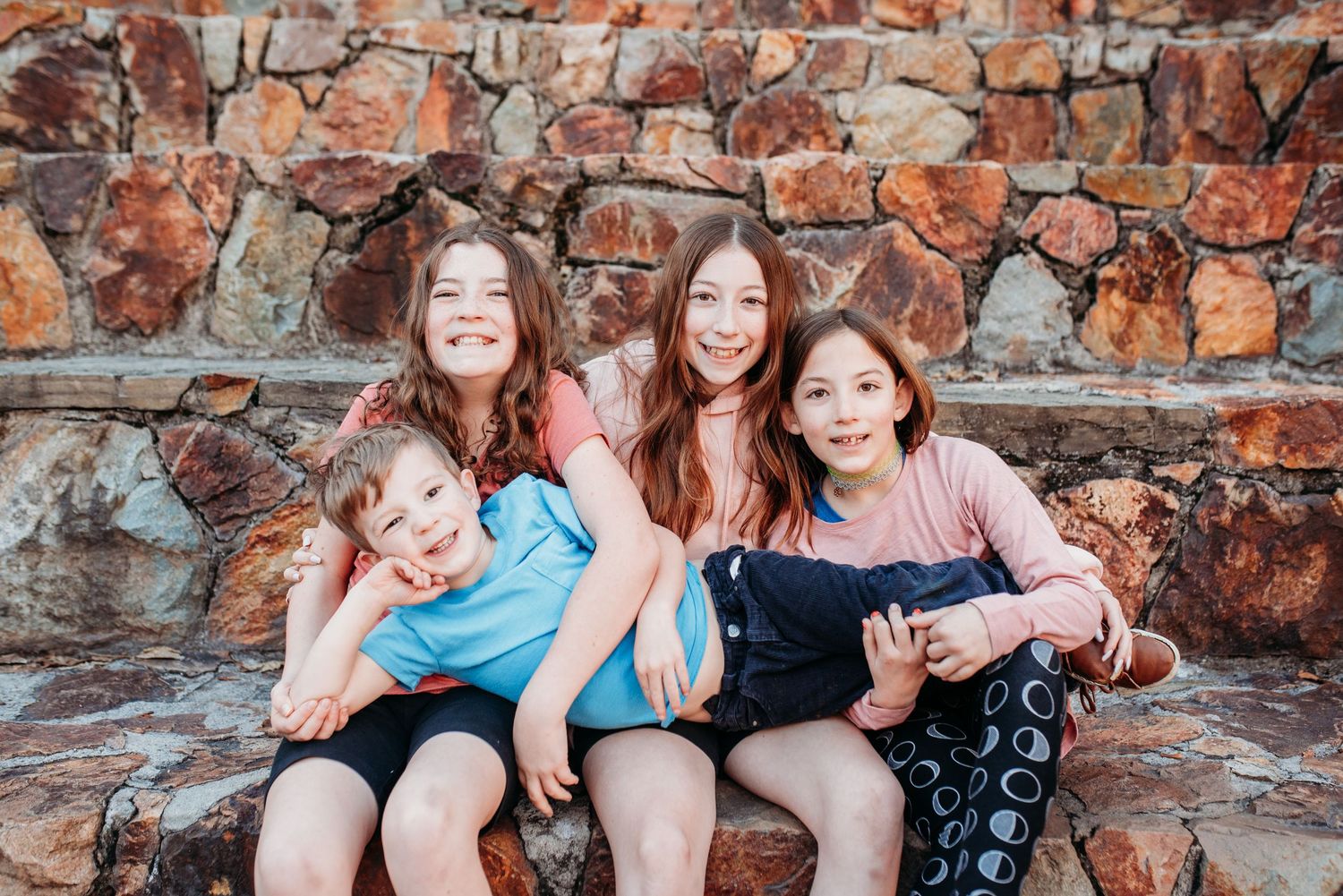 Group sitting together against a rustic stone wall background during an outdoor photo session.