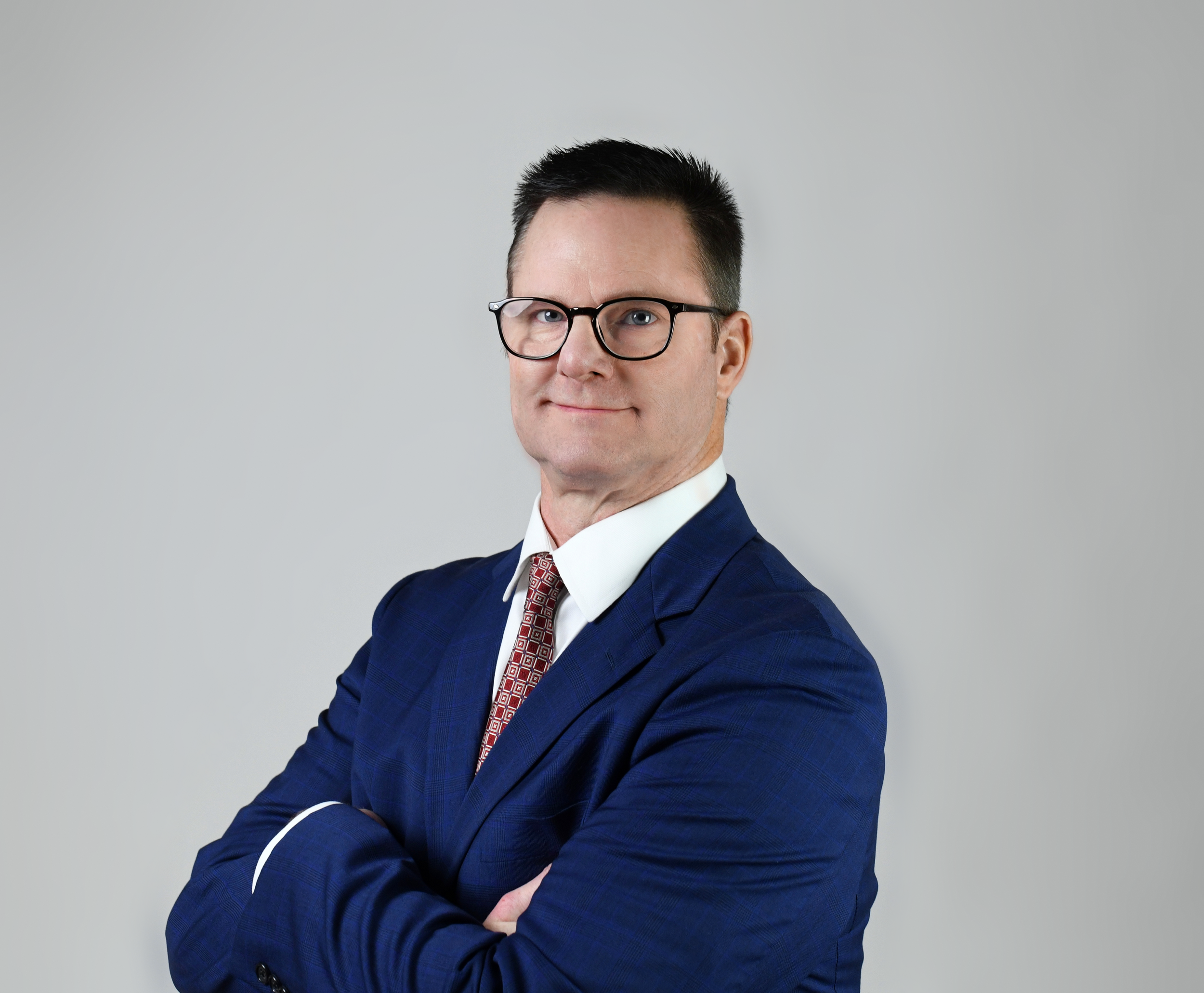 Professional in navy suit and glasses stands confidently with arms crossed.