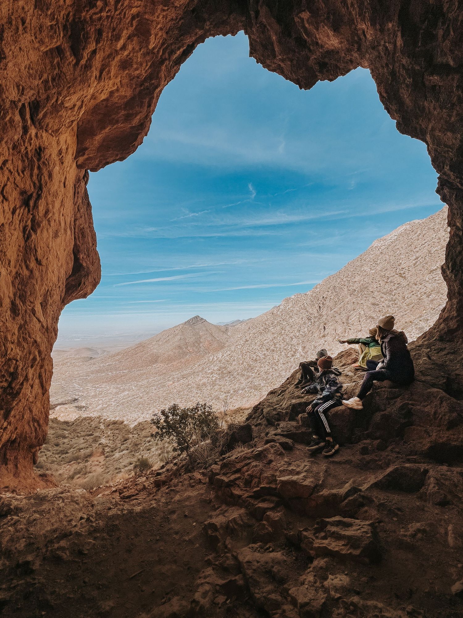 View through natural rock arch showing desert landscape and people resting in cave entrance.