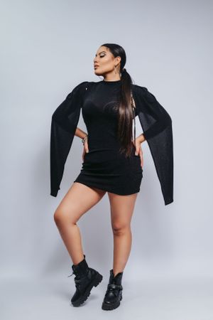 Model in black mini dress and combat boots strikes dramatic pose against light background.