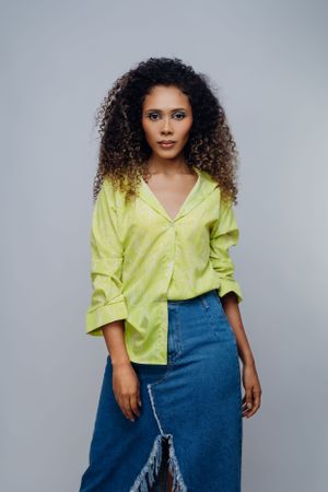 Fashion model wearing lime green button-up shirt and denim skirt poses against grey background.