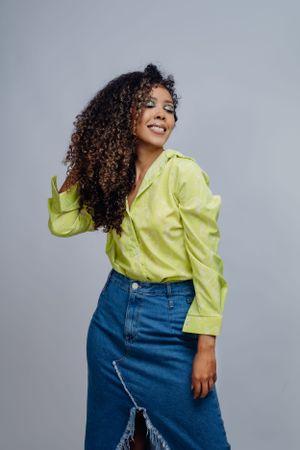 Casual fashion portrait with bright yellow shirt and blue denim skirt against grey background.