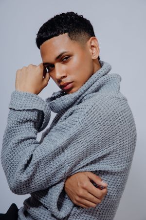 Model wearing chunky grey knit sweater poses against light background.