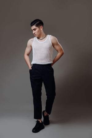 Fashion model wearing white tank top and black pants in minimal studio setting.