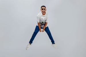 Energetic pose in white t-shirt with animal graphic, blue jeans and white sneakers against grey background.