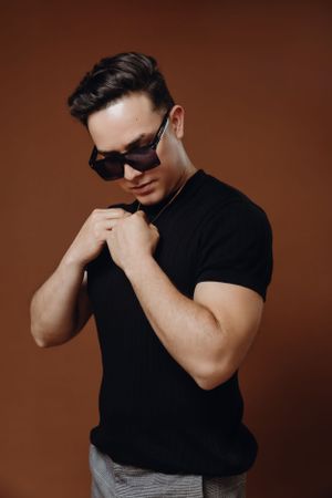 Stylish pose in black polo shirt and sunglasses against brown background.