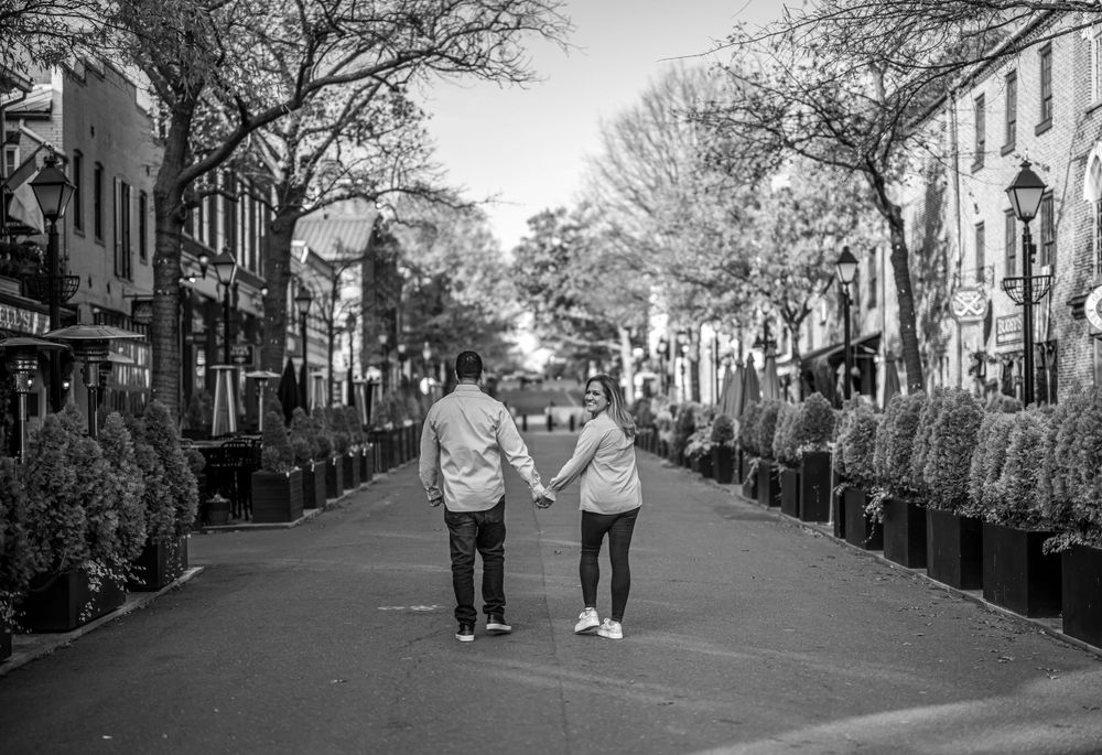 Black and white photo of a couple walking down a tree-lined historic street.