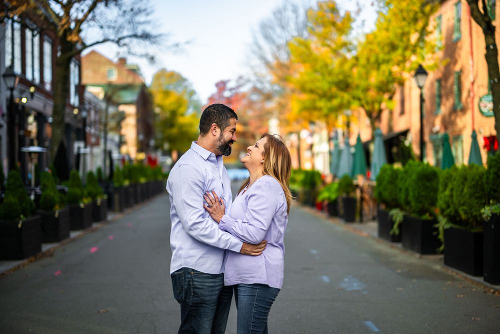 Couple sharing intimate moment on scenic street with fall foliage and decorative planters.