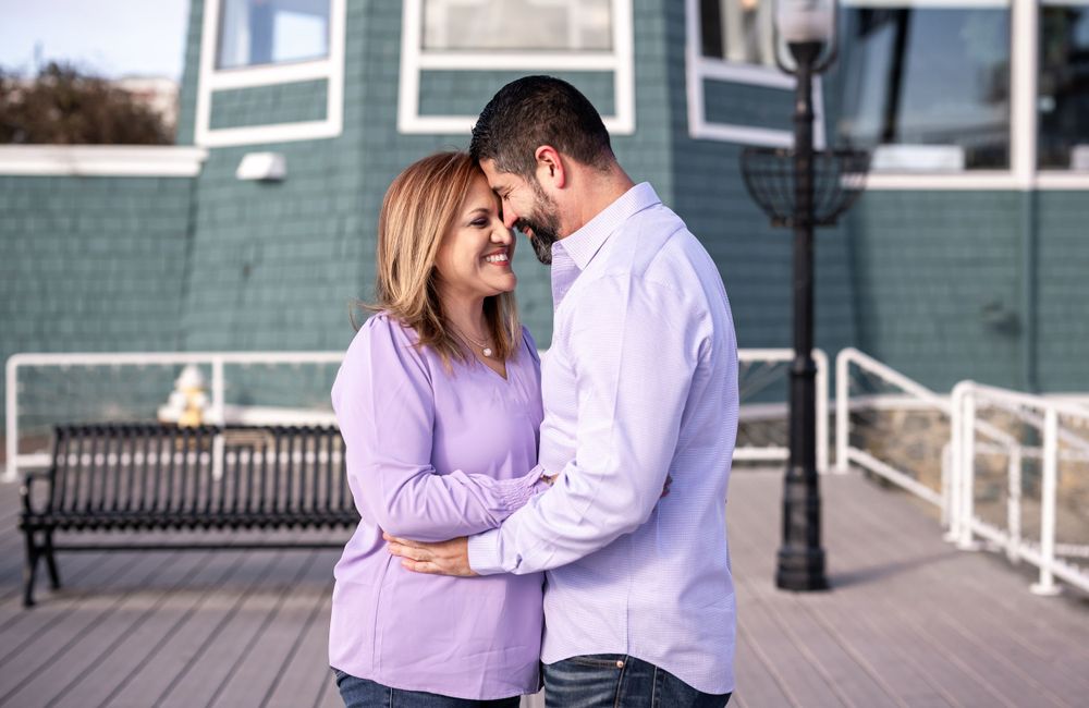 Couple sharing tender moment outside teal-colored coastal building on wooden deck.