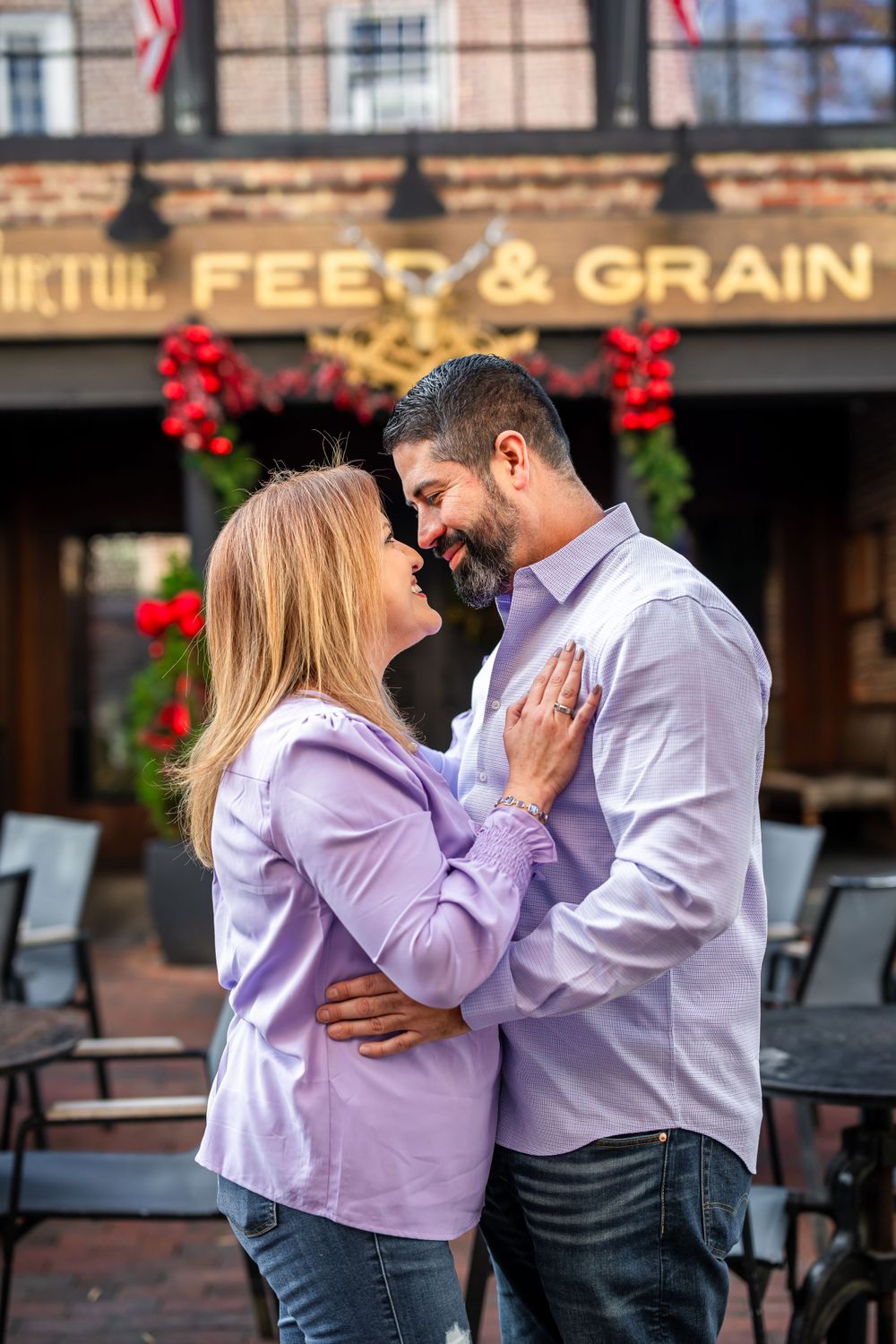 Couple in casual attire sharing a romantic moment outside Feed & Grain building with festive decor.