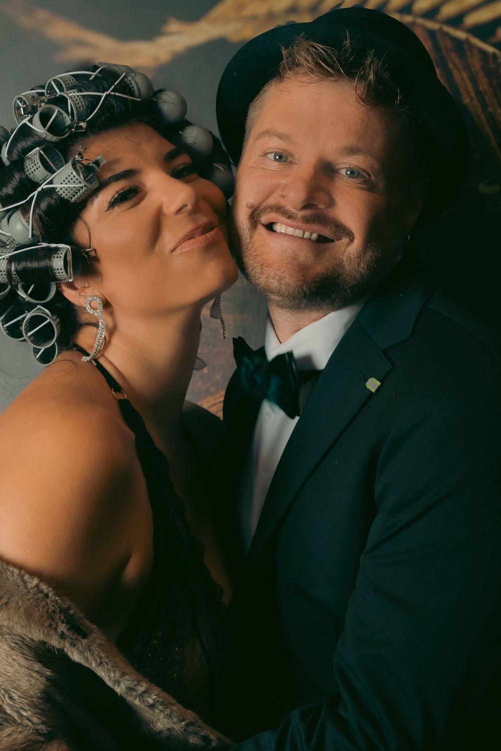 Businessfotografie, Business Project. Elegant couple in formal attire sharing an intimate moment against palm leaf backdrop.